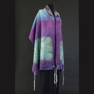May include: A purple and blue silk tallit with a gold and teal design. The tallit has white tzitzit.