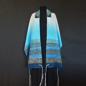 May include: A blue and white prayer shawl with gold embroidery. The shawl has a gradient design, with the blue color fading to white. The embroidery features intricate patterns and designs.