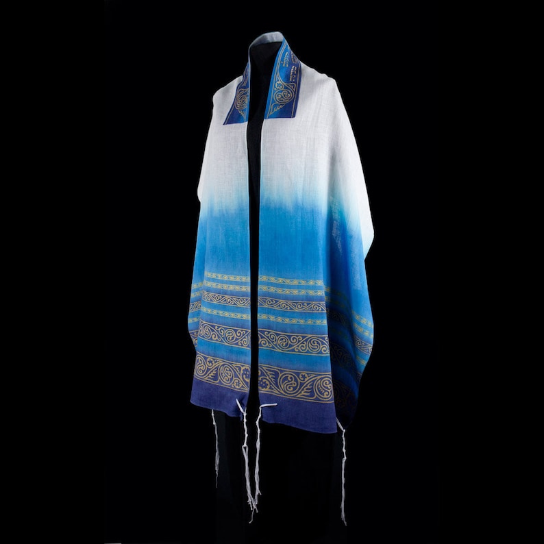 May include: A blue and white prayer shawl with gold embroidery. The shawl has a gradient design, with the top being white and the bottom being blue. The shawl is decorated with gold embroidery, which includes a pattern of vines and leaves.