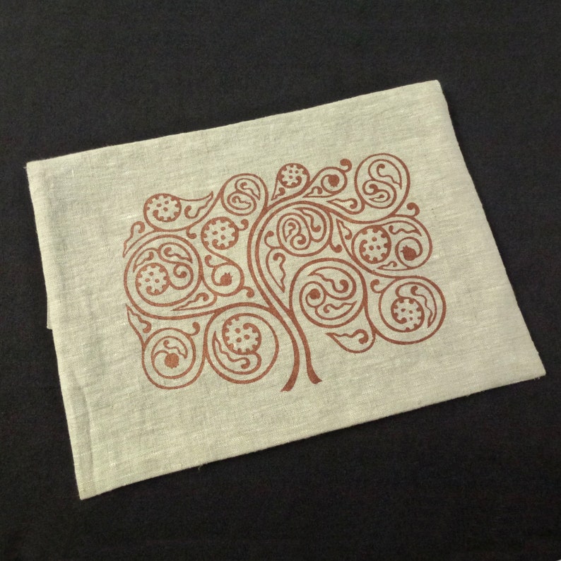 May include: A light beige linen tea towel with a brown tree design. The tree is made up of swirling, paisley-like shapes.
