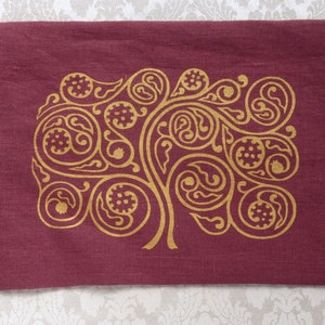 May include: A burgundy linen pillow with a gold embroidered design of a stylized tree with swirling branches and leaves.
