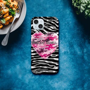 Op de afbeelding: Een smartphonehoesje met een zwart-wit zebraprintpatroon en een roze camouflagehart. De tekst "RESILIENT AS HELL" staat op het hart gedrukt. De hoes heeft een camera-uitsparing.