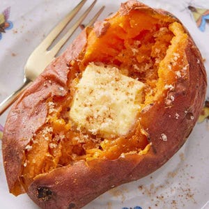 Può includere: Una patata dolce al forno, tagliata e condita con un quadrato di burro, è adagiata su un piatto decorativo. Il piatto ha un disegno a farfalla. Una forchetta dorata è appoggiata sul piatto accanto alla patata. La patata è di un arancione vibrante.