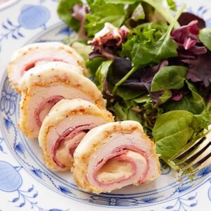 May include: Sliced chicken breast rolls filled with ham and cheese, served with a fresh green salad on a decorative blue and white plate. A gold fork rests on the plate, ready to enjoy the meal.