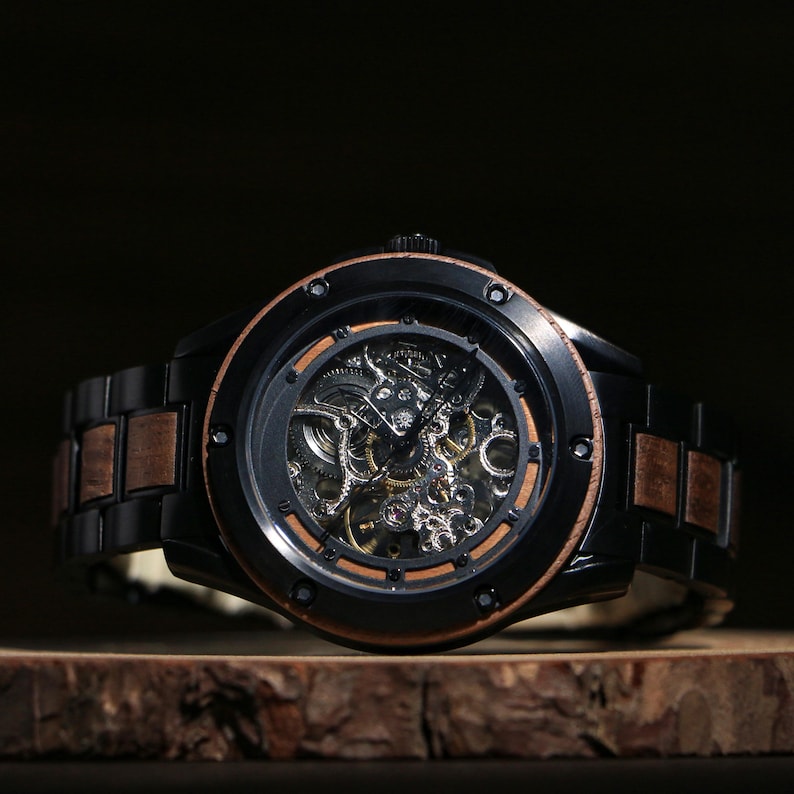 May include: A black skeleton watch with a wooden strap and a brown bezel. The watch face reveals the intricate inner workings of the mechanical movement. The watch is displayed on a wooden surface.
