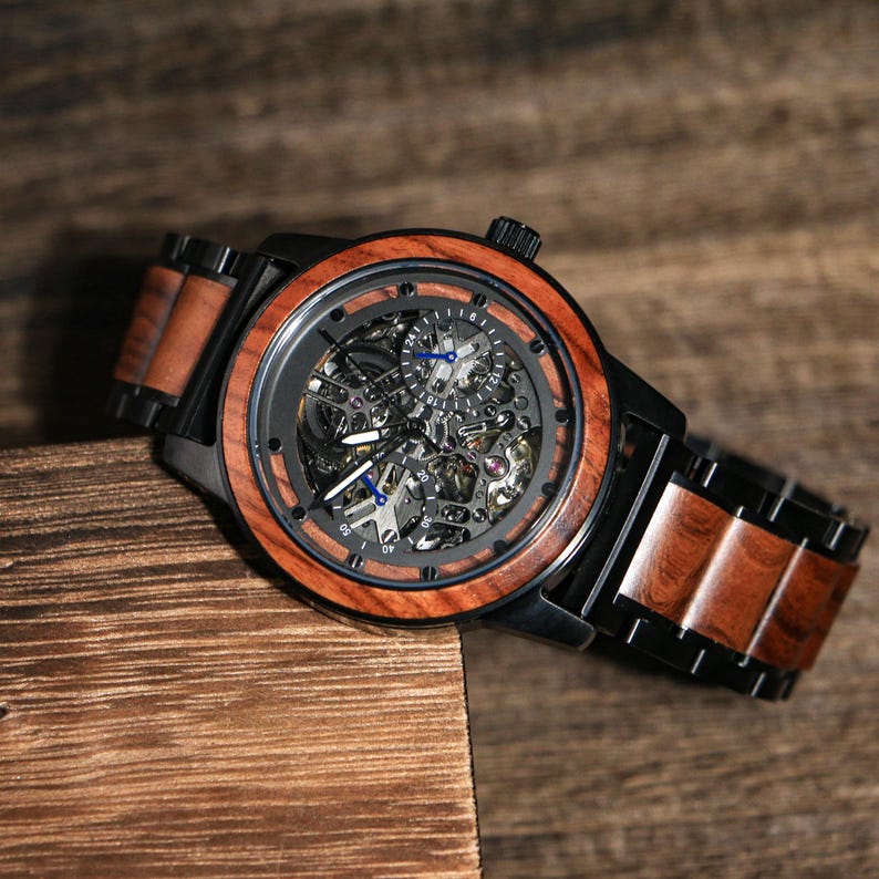 May include: A wooden wristwatch with a black case and a skeleton dial. The watch has a brown wooden bezel and strap, with blue hands and markers. The watch is displayed on a wooden surface.