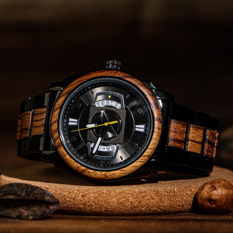 K&ouml;nnte beinhalten: Eine schwarze Armbanduhr mit Holzl&uuml;nette und -armband. Das Zifferblatt der Uhr ist schwarz mit wei&szlig;en und gelben Akzenten. Die Uhr liegt auf einer Holzoberfl&auml;che.