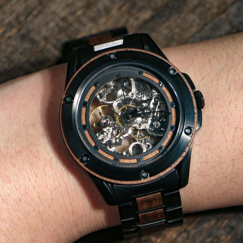 May include: A black wristwatch with a skeleton dial, revealing the internal mechanisms. The watch has a brown wooden bezel and band details. The watch is on a wrist.