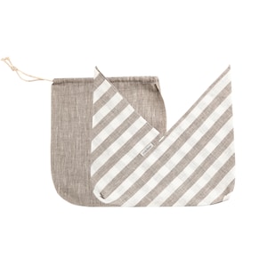 May include: Two linen bags are shown. One is a drawstring bag in a solid taupe colour. The other is a flat bag with wide, vertical stripes in taupe and white. The bags are made of a natural, textured fabric.