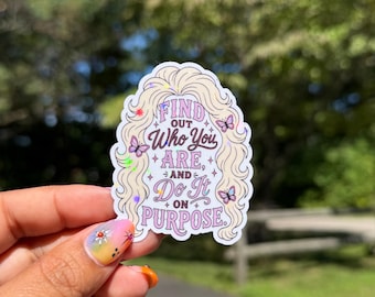 May include: A die-cut sticker featuring a stylized illustration of blonde hair framing the text "FIND OUT Who You ARE, AND Do It ON PURPOSE." The design includes small purple butterflies and holographic star accents on a white background.