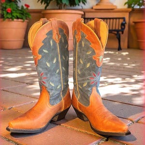 May include: A pair of brown and blue cowboy boots. The boots have a pointed toe and a decorative floral pattern on the shaft. The boots are made of leather and have a stacked heel.