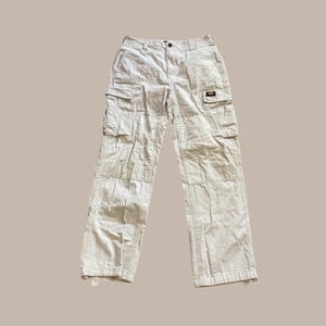 Könnte beinhalten: Cremefarbene Cargohose mit mehreren Taschen an den Beinen und einem kleinen rechteckigen Aufnäher. Die Hose hat einen Knopf- und Reißverschluss und ist aus strapazierfähigem Stoff gefertigt. Die Hose ist neutralfarben und für verschiedene Outfits geeignet.