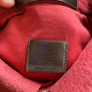 May include: Close-up of a red Nike Fit Dry polo shirt. The shirt's collar and tag are visible. The tag reads "MADE IN CHINA FABRIQUE EN CHINE" and "Nike Fit Dry".