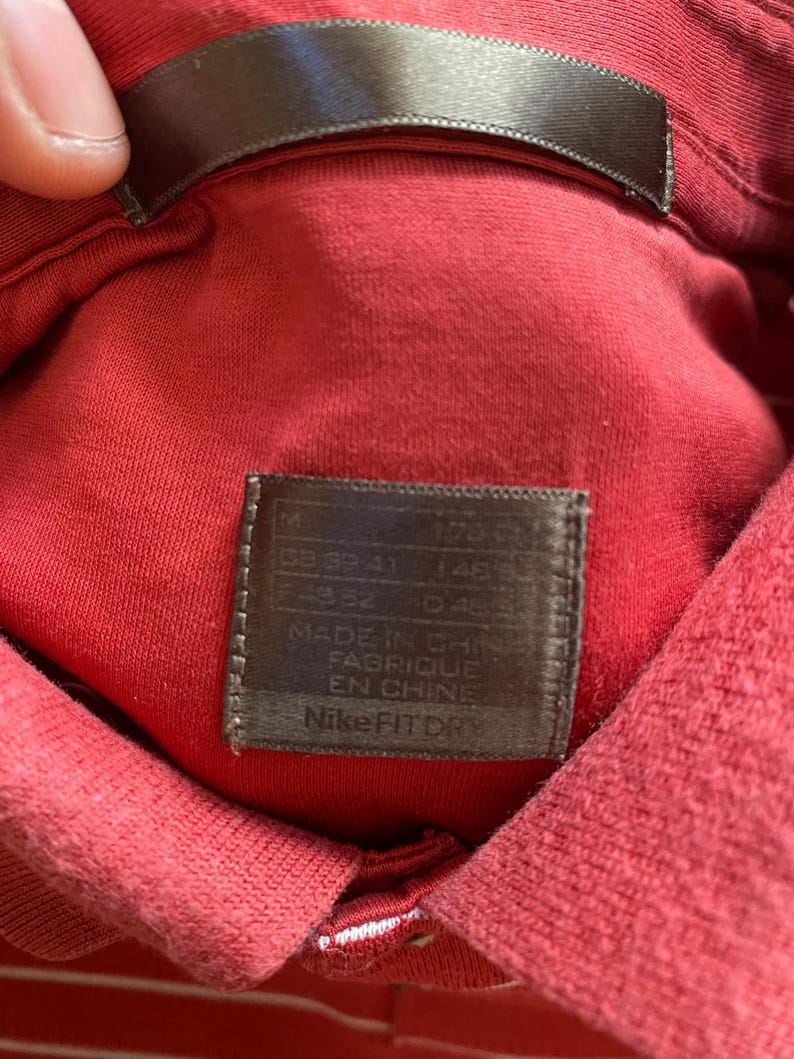 May include: Close-up of a red Nike Fit Dry polo shirt. The shirt's collar and tag are visible. The tag reads "MADE IN CHINA FABRIQUE EN CHINE" and "Nike Fit Dry".