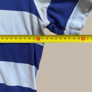 K&ouml;nnte beinhalten: Ein blau-wei&szlig; gestreiftes Hemd mit einem gelben Ma&szlig;band dar&uuml;ber. Das Band misst etwa 46 cm &uuml;ber dem Hemd. Das Hemd hat kurze &Auml;rmel und einen hellen Hintergrund.