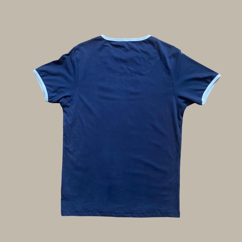 Puede incluir: Camiseta azul marino con ribete azul claro en el cuello y las mangas. La camiseta de manga corta est&aacute; hecha de un material suave. La camiseta es una prenda informal.