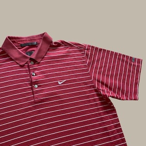 May include: A maroon polo shirt with white horizontal stripes. The shirt has a collar, three buttons, and short sleeves. A small white Nike swoosh logo is visible on the chest.