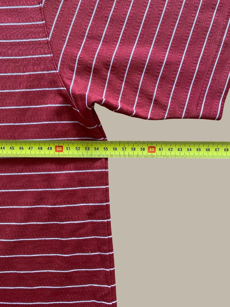May include: A maroon and white striped short-sleeve shirt. The shirt has horizontal stripes on the lower portion and vertical stripes on the upper portion. A yellow measuring tape is placed across the bottom of the shirt.
