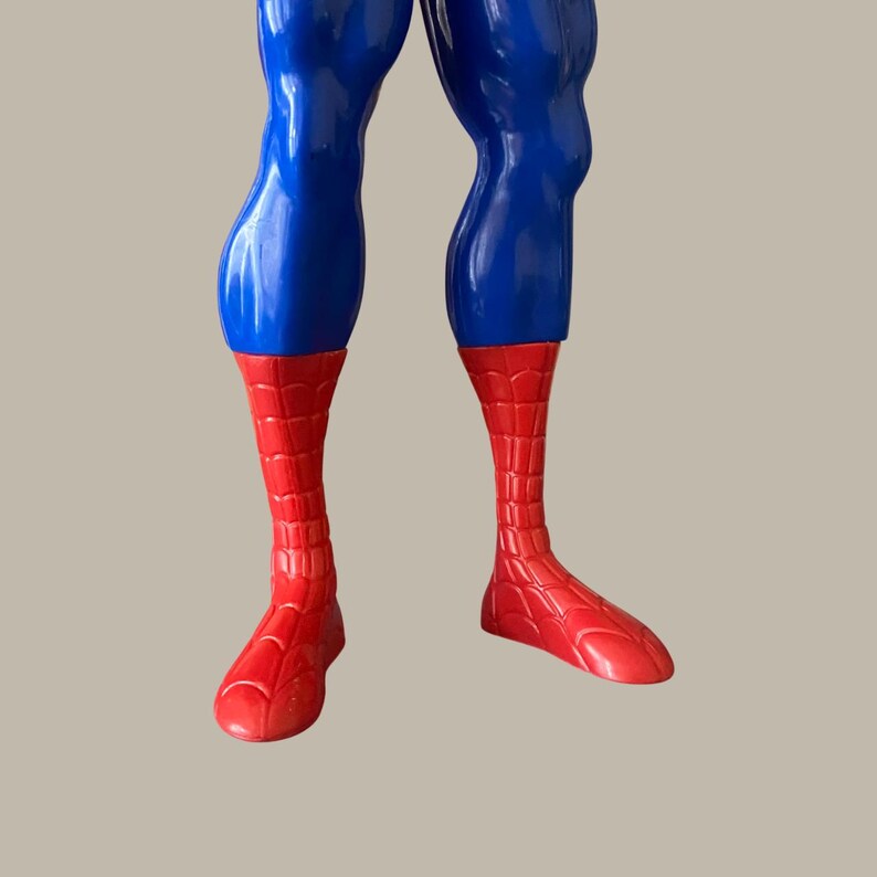 Puede incluir: Primer plano de la parte inferior del cuerpo de una figura de acci&oacute;n de Spider-Man. Las piernas de la figura son azules, que pasan a pies y pantorrillas rojas con un patr&oacute;n de telara&ntilde;a. La figura est&aacute; sobre un fondo neutro.