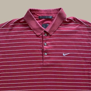 May include: Maroon polo shirt with white horizontal stripes. Features a collared neckline, three-button placket, and a small Nike logo on the chest. The shirt has a classic, sporty design.