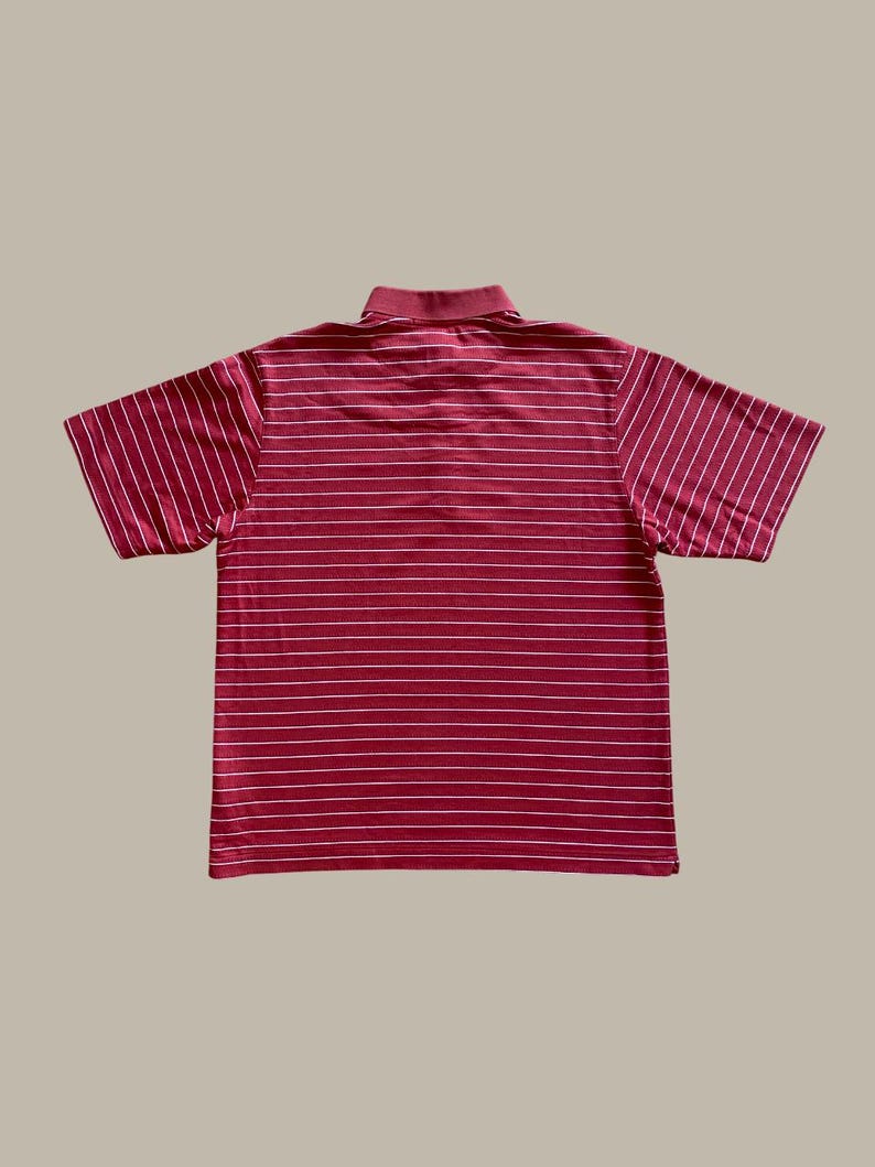 May include: A maroon polo shirt with white horizontal stripes. The short-sleeved shirt has a collared neckline and is made of a ribbed fabric. The shirt is laid flat on a neutral background.