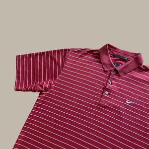 May include: Maroon polo shirt with white horizontal stripes. The shirt has a collared neckline with three buttons and a small Nike logo on the chest. The short sleeves are visible.