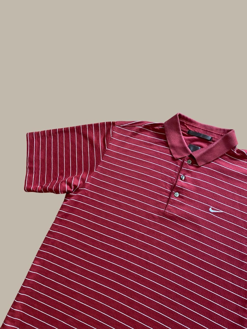 May include: Maroon polo shirt with white horizontal stripes. The shirt has a collared neckline with three buttons and a small Nike logo on the chest. The short sleeves are visible.