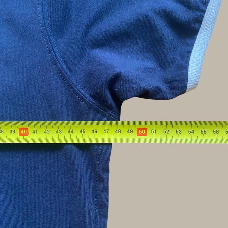 Puede incluir: Una camiseta azul marino con un ribete blanco en la manga. Una cinta m&eacute;trica amarilla se coloca sobre la camiseta, mostrando medidas de 96.5 cm a 142.2 cm.