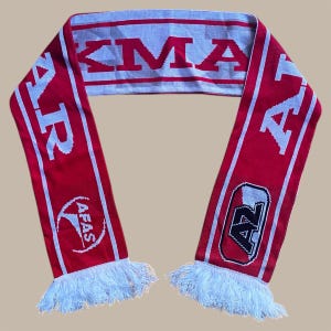 May include: A red and white knitted scarf with the text "AZ" and "AFAS" in white. The scarf has white fringe at both ends. The scarf is a fan accessory.