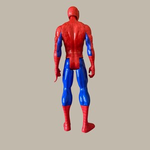 Puede incluir: Una figura de acci&oacute;n de Spider-Man roja, azul y negra, vista desde atr&aacute;s. La figura tiene cabeza y torso rojos, piernas y brazos azules, y pies y manos rojos. La figura est&aacute; de pie.