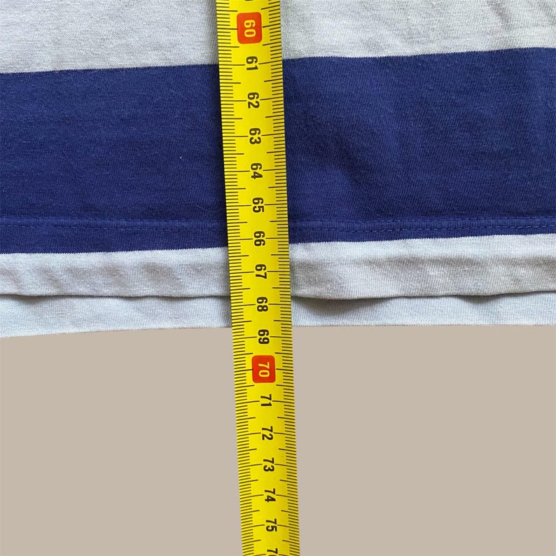 K&ouml;nnte beinhalten: Nahaufnahme eines grau-blau gestreiften Hemdes. Ein gelbes Ma&szlig;band wird vertikal am Hemd platziert und zeigt Messungen von 152 bis 190 cm.