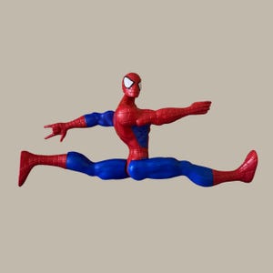 Puede incluir: Figura de acci&oacute;n de Spider-Man rojo y azul en pose de apertura de piernas. La figura tiene un torso y cabeza rojos con detalles de ojos blancos, y piernas y brazos azules. La figura est&aacute; en una posici&oacute;n din&aacute;mica y extendida.