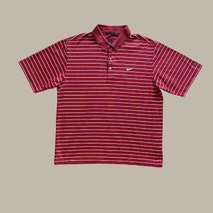 May include: A short-sleeved polo shirt in a deep red hue, featuring horizontal white stripes. The shirt has a collared neckline, a three-button placket, and a small Nike logo on the chest. The overall design is classic and sporty.