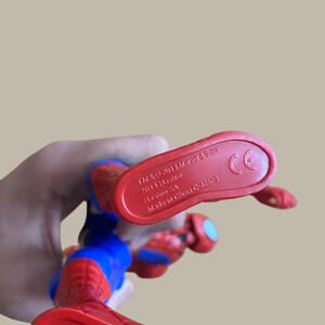 Puede incluir: Figura de acci&oacute;n de Spider-Man rojo y azul. Se ve el pie de la figura, con el texto "TM & &copy; 2013 Marvel & Subs, 2013 Hasbro, Hasbro SA, Made in China, C32528" y una marca CE.