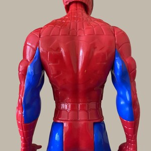 Puede incluir: Figura de acci&oacute;n de Spider-Man roja y azul, vista desde atr&aacute;s. La figura tiene un torso y cabeza rojos con un patr&oacute;n texturizado, y brazos y piernas azules. Es un juguete.
