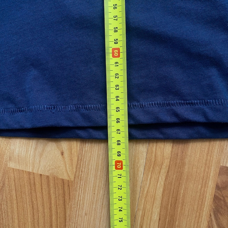 Puede incluir: Una tela azul marino se mide con una cinta m&eacute;trica amarilla y negra. La cinta muestra medidas de 142 a 190 cm. La tela est&aacute; sobre una superficie de madera.