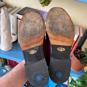 Puede incluir: Un par de zapatos de vestir de cuero burdeos, suelas hacia arriba. Las suelas muestran signos de desgaste. Los tacones son de goma negra con la marca "TINDRO" en un c&iacute;rculo azul. Estilo cl&aacute;sico, probablemente vintage.