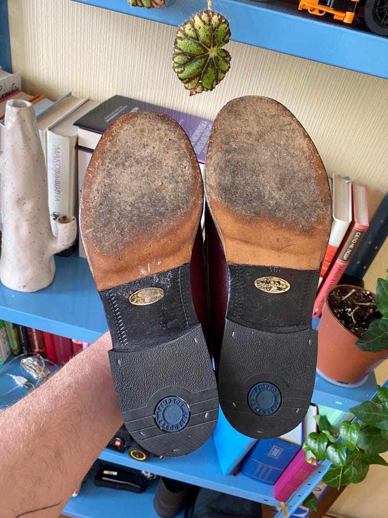 Puede incluir: Un par de zapatos de vestir de cuero burdeos, suelas hacia arriba. Las suelas muestran signos de desgaste. Los tacones son de goma negra con la marca "TINDRO" en un c&iacute;rculo azul. Estilo cl&aacute;sico, probablemente vintage.