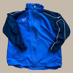 May include: A blue and navy athletic jacket with a full zipper closure. The jacket features white trim along the sleeves and shoulders, and a small Nike logo on the chest. The jacket has a high collar and elastic cuffs.