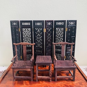May include: A miniature wooden furniture set comprising two chairs and a small table, all finished in dark brown. Behind them is a decorative folding screen with intricate cut-out patterns. The set is displayed on a wooden tray.