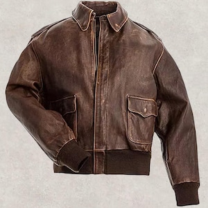 Könnte beinhalten: Braune Leder-Bomberjacke mit Reißverschluss, zwei Vordertaschen und geripptem Kragen und Bündchen. Die Jacke hat ein klassisches Design und einen Vintage-Look.