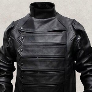 May include: A black leather jacket with a high collar and multiple horizontal chest pockets. The jacket features a unique design with decorative stitching and button details, and a zipper on the right side.
