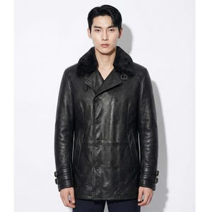 May include: A black leather double-breasted jacket with a shearling collar. The jacket has a classic design with multiple buttons and buckle details on the sleeves. The model is wearing the jacket against a white background.