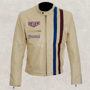 Puede incluir: Chaqueta de cuero color crema con cuello negro y cremallera frontal. Cuenta con un parche con el logo "HEUER", un parche "Firestone" y rayas verticales azules y burdeos. Una chaqueta clásica de estilo racing.