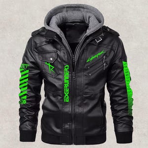 May include: Black faux leather jacket with a gray hooded insert. The jacket features green "Cyberpunk" and "Edgerunners" text and graphics. Includes two chest pockets, a zip closure, and a ribbed cuff.