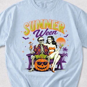 Op de afbeelding: Lichtblauw T-shirt met een afbeelding van een skelet en een vrouw die ontspannen op een bank zitten met cocktails, een pompoen en de tekst "Summer Ween". Het ontwerp bevat vleermuizen, palmbomen en een zonsondergang.