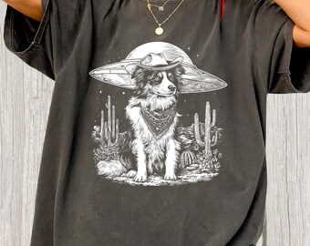 May include: Dark gray t-shirt featuring a graphic of a dog wearing a cowboy hat and bandana, with a UFO-shaped hat. The dog is set against a desert landscape with cacti. The word "Pepper" is printed at the bottom.
