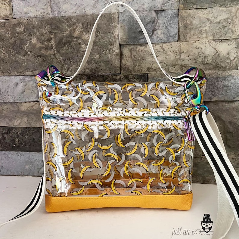 May include: Clear plastic tote bag with a yellow bottom and a black and white striped strap. The bag has a banana print.