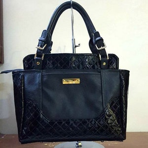 Könnte beinhalten: Schwarze gesteppte Handtasche mit goldenen Beschlägen und einem goldenen Logo mit der Aufschrift "D'rose".