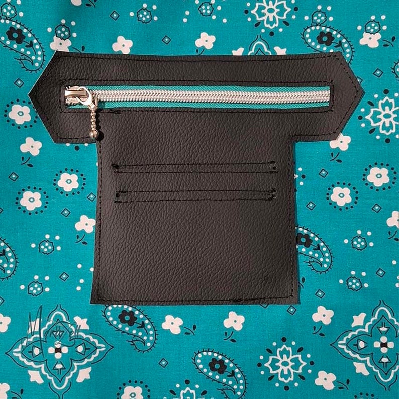 Puede incluir: Un panel de bolsillo de piel sint&eacute;tica negra con una cremallera horizontal plateada con ribete de tela verde azulado, unido a un fondo de tela verde azulado con un patr&oacute;n floral y de cachemira blanco. El bolsillo incluye dos ranuras.